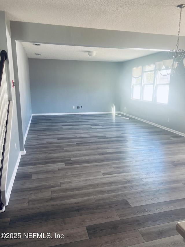 empty room featuring dark hardwood / wood-style flooring, a textured ceiling, and an inviting chandelier