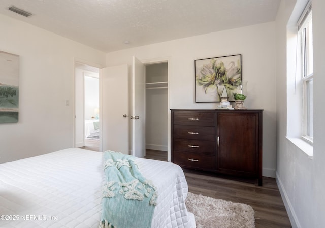 bedroom with multiple windows, dark wood-type flooring, a textured ceiling, and a closet