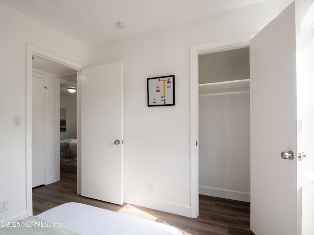 unfurnished bedroom featuring a spacious closet, a textured ceiling, dark hardwood / wood-style flooring, and a closet