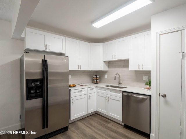 kitchen featuring sink, white cabinetry, tasteful backsplash, wood-type flooring, and appliances with stainless steel finishes