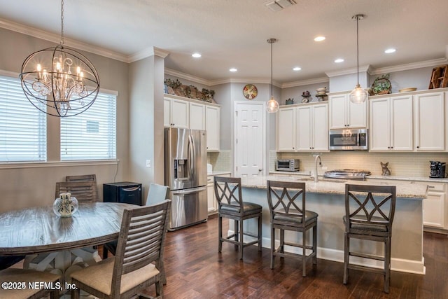 kitchen with hanging light fixtures, appliances with stainless steel finishes, a center island with sink, and light stone counters