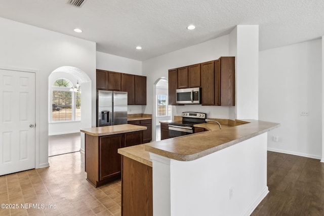 kitchen featuring dark brown cabinetry, a center island, a textured ceiling, kitchen peninsula, and stainless steel appliances