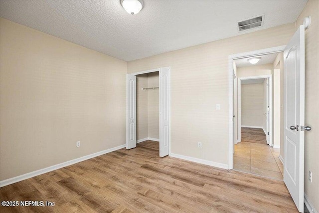 unfurnished bedroom featuring a closet, a textured ceiling, and light wood-type flooring