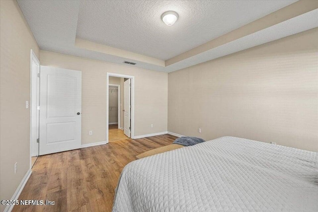 bedroom with a raised ceiling, a textured ceiling, and light hardwood / wood-style flooring