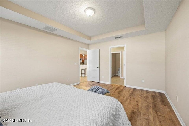 bedroom with a raised ceiling, hardwood / wood-style flooring, and a textured ceiling