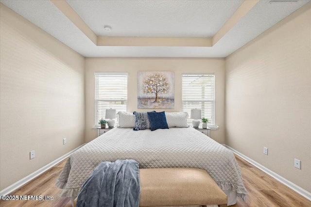 bedroom with wood-type flooring, a raised ceiling, and a textured ceiling