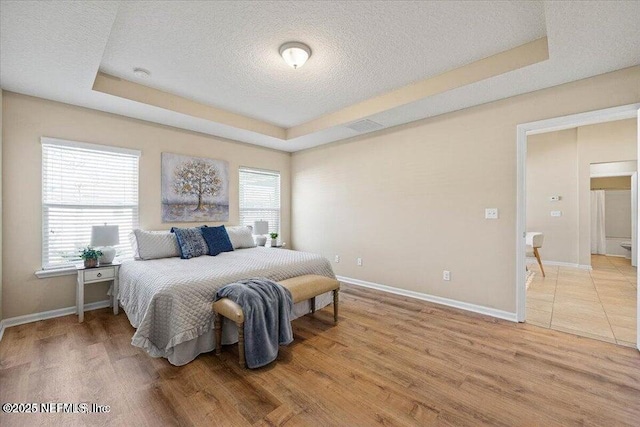 bedroom with a tray ceiling, wood-type flooring, and a textured ceiling