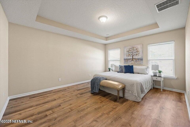 bedroom featuring multiple windows, hardwood / wood-style floors, a tray ceiling, and a textured ceiling