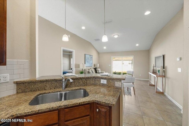 kitchen with light stone countertops, lofted ceiling, sink, and pendant lighting