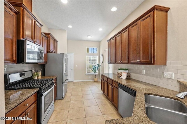 kitchen featuring appliances with stainless steel finishes, sink, light tile patterned floors, and dark stone counters