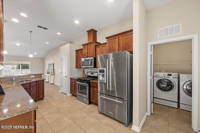 kitchen with pendant lighting, sink, appliances with stainless steel finishes, light stone countertops, and washing machine and clothes dryer