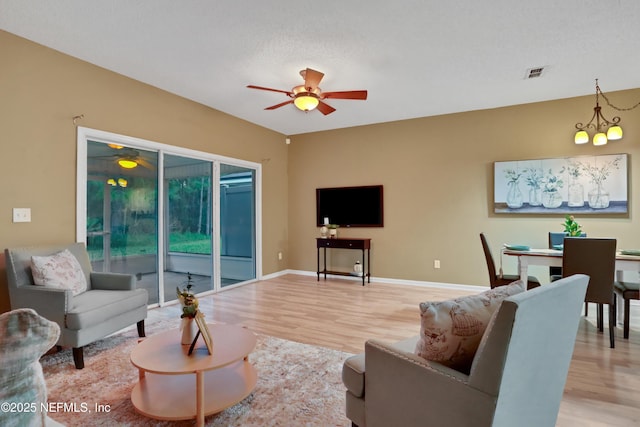 living room with ceiling fan with notable chandelier, light hardwood / wood-style floors, and a textured ceiling