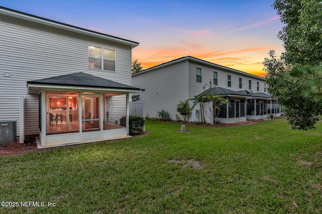 back house at dusk featuring a lawn and a sunroom