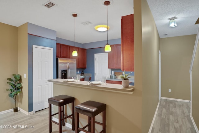 kitchen featuring stainless steel refrigerator with ice dispenser, a kitchen bar, hanging light fixtures, light hardwood / wood-style flooring, and kitchen peninsula