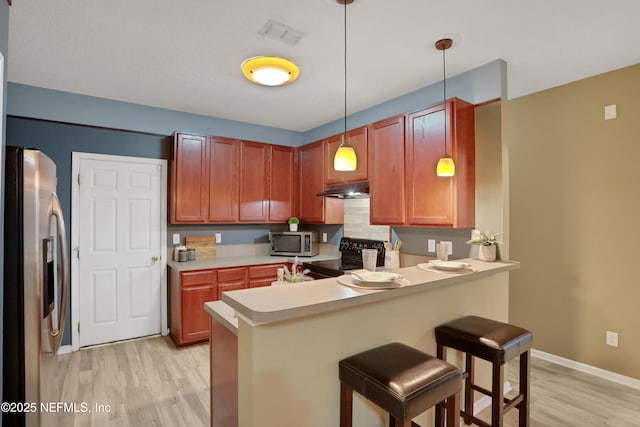 kitchen with appliances with stainless steel finishes, a kitchen breakfast bar, kitchen peninsula, pendant lighting, and light hardwood / wood-style floors