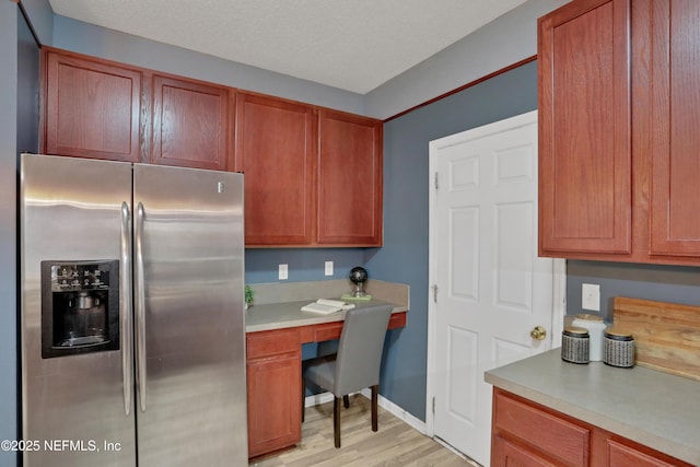 kitchen with light wood-type flooring, built in desk, a textured ceiling, and stainless steel refrigerator with ice dispenser