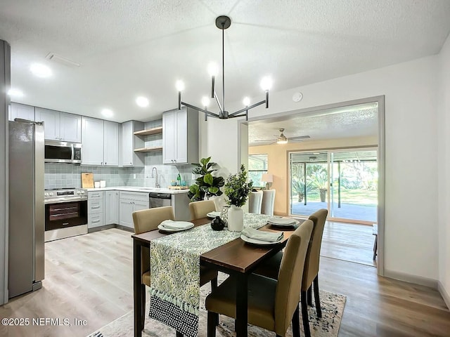 dining room with ceiling fan, sink, a textured ceiling, and light wood-type flooring