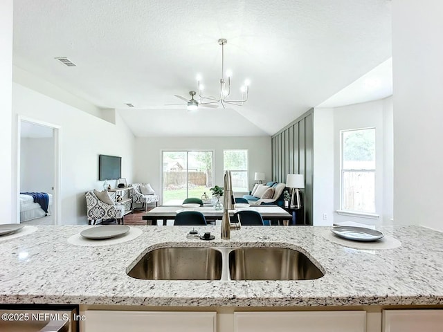 kitchen with pendant lighting, lofted ceiling, light stone countertops, and sink