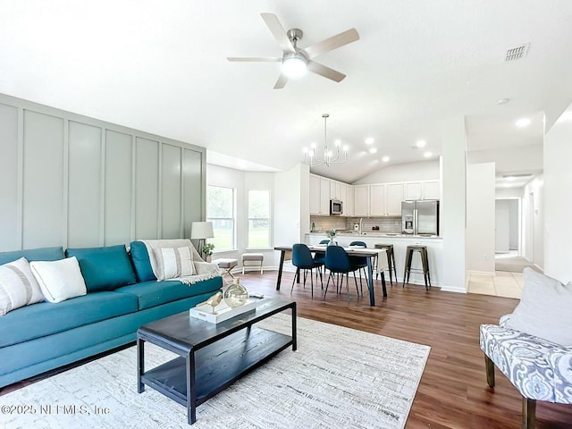 living room featuring vaulted ceiling, ceiling fan with notable chandelier, and light hardwood / wood-style flooring