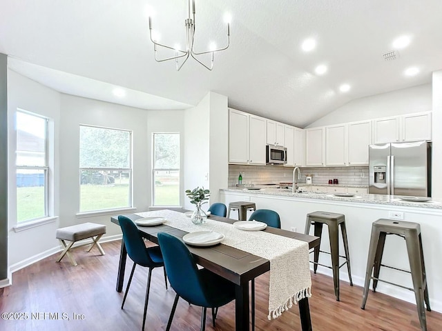 dining area featuring lofted ceiling, sink, a notable chandelier, and wood-type flooring