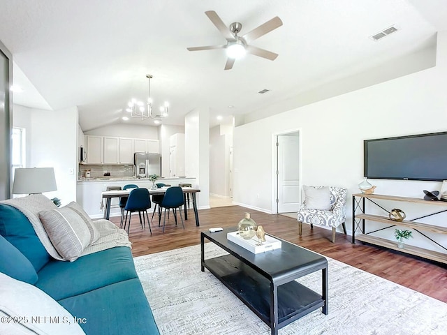 living room featuring vaulted ceiling, ceiling fan with notable chandelier, and light wood-type flooring