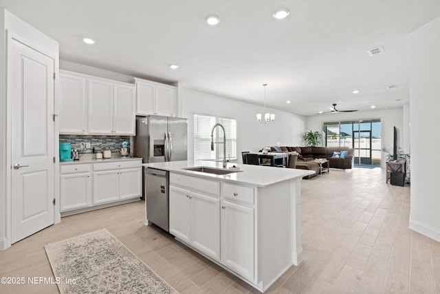 kitchen with stainless steel appliances, a kitchen island with sink, sink, and white cabinets