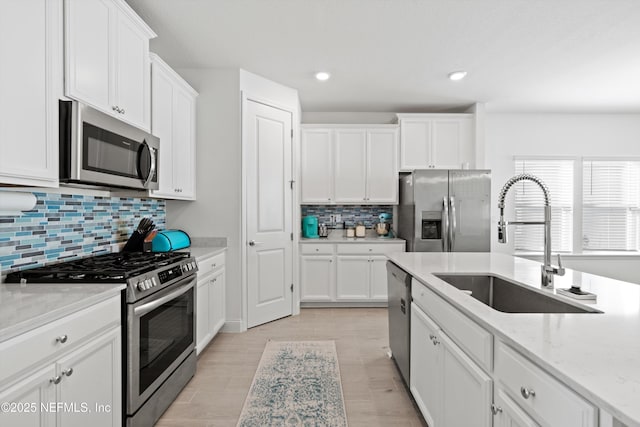 kitchen featuring sink, appliances with stainless steel finishes, light stone counters, tasteful backsplash, and white cabinets