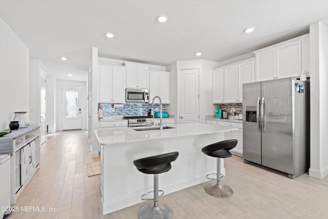 kitchen featuring stainless steel appliances, white cabinetry, a breakfast bar, and light hardwood / wood-style floors