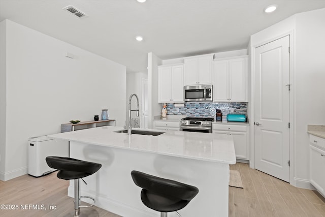 kitchen featuring sink, a center island with sink, appliances with stainless steel finishes, a kitchen breakfast bar, and white cabinets