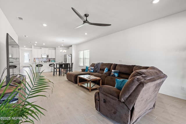 living room featuring ceiling fan with notable chandelier, a healthy amount of sunlight, and light wood-type flooring