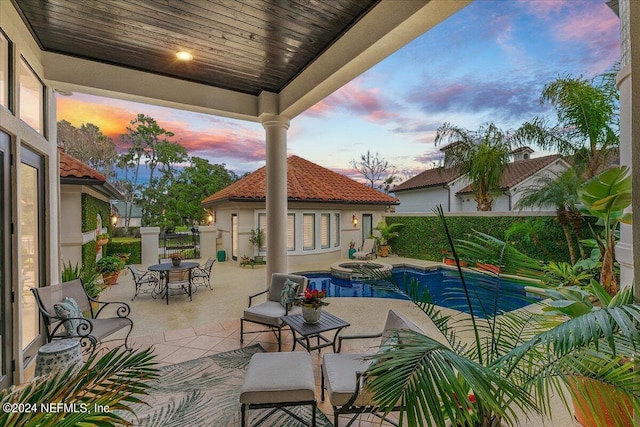 pool at dusk featuring an in ground hot tub and a patio area