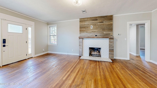 unfurnished living room featuring ornamental molding, a brick fireplace, a textured ceiling, and light hardwood / wood-style floors