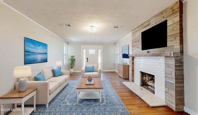 living room featuring a brick fireplace, wood-type flooring, ornamental molding, and a textured ceiling