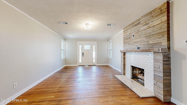 unfurnished living room with a brick fireplace, ornamental molding, a textured ceiling, and light wood-type flooring