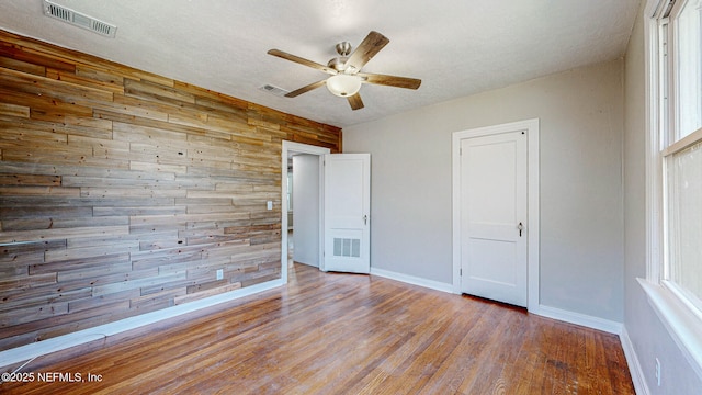 unfurnished bedroom with ceiling fan, wooden walls, a textured ceiling, and light wood-type flooring