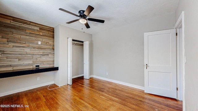 unfurnished bedroom with hardwood / wood-style flooring, ceiling fan, wooden walls, and a closet