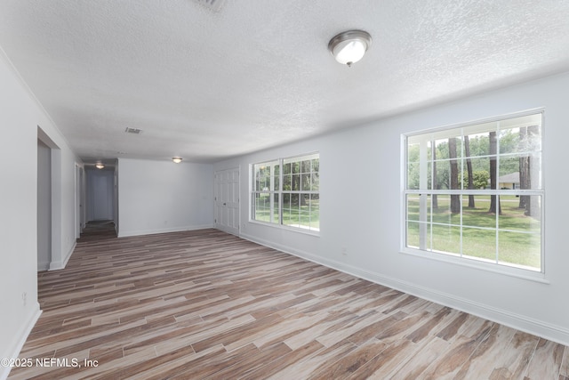 empty room with a textured ceiling and light hardwood / wood-style flooring