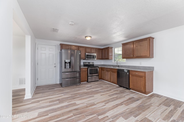 kitchen featuring stainless steel appliances, sink, a textured ceiling, and light hardwood / wood-style flooring