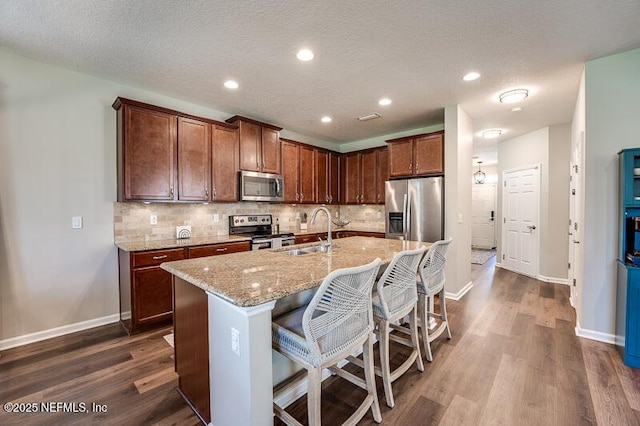 kitchen featuring an island with sink, sink, a kitchen bar, light stone counters, and stainless steel appliances