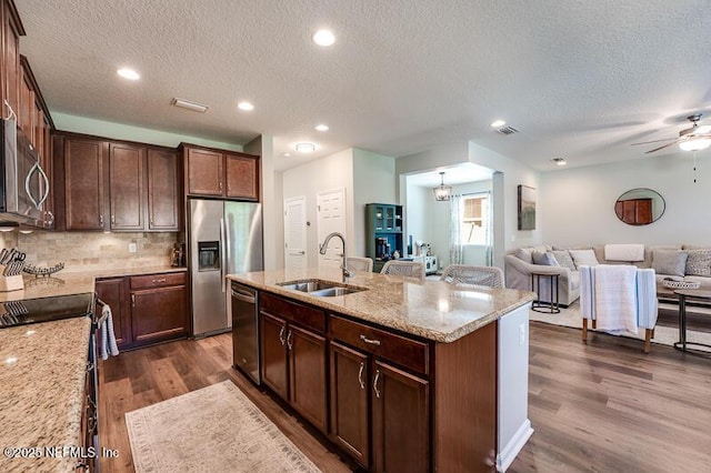 kitchen featuring sink, stainless steel appliances, light stone counters, a center island with sink, and dark hardwood / wood-style flooring