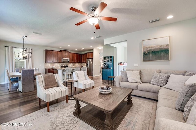 living room featuring wood-type flooring, ceiling fan with notable chandelier, and a textured ceiling