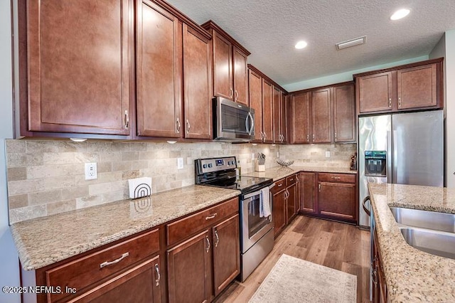 kitchen featuring appliances with stainless steel finishes, light wood-type flooring, backsplash, light stone countertops, and a textured ceiling