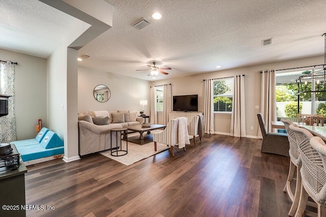 living room with ceiling fan with notable chandelier, dark wood-type flooring, and a textured ceiling