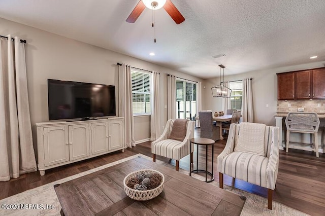 living room featuring dark hardwood / wood-style flooring, ceiling fan with notable chandelier, and a textured ceiling