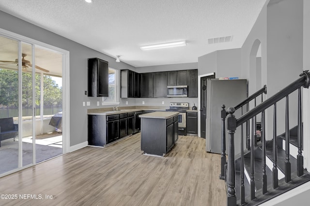 kitchen with light hardwood / wood-style flooring, a kitchen island, a textured ceiling, and appliances with stainless steel finishes