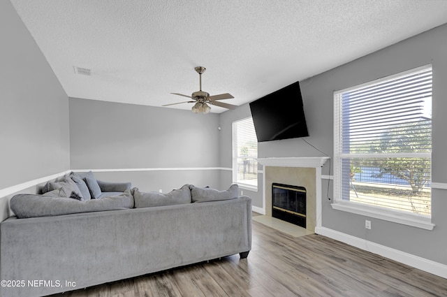 living room with ceiling fan, a high end fireplace, light hardwood / wood-style floors, and a textured ceiling