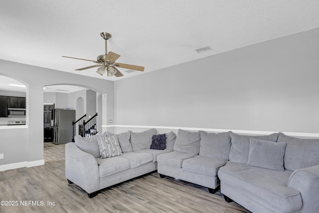 living room with ceiling fan, light hardwood / wood-style flooring, and a textured ceiling