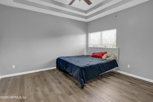 bedroom featuring hardwood / wood-style floors, a raised ceiling, and ceiling fan