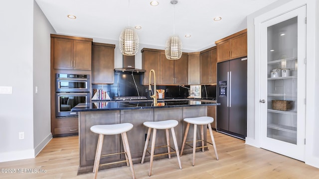 kitchen with a breakfast bar, hanging light fixtures, a center island with sink, light wood-type flooring, and appliances with stainless steel finishes