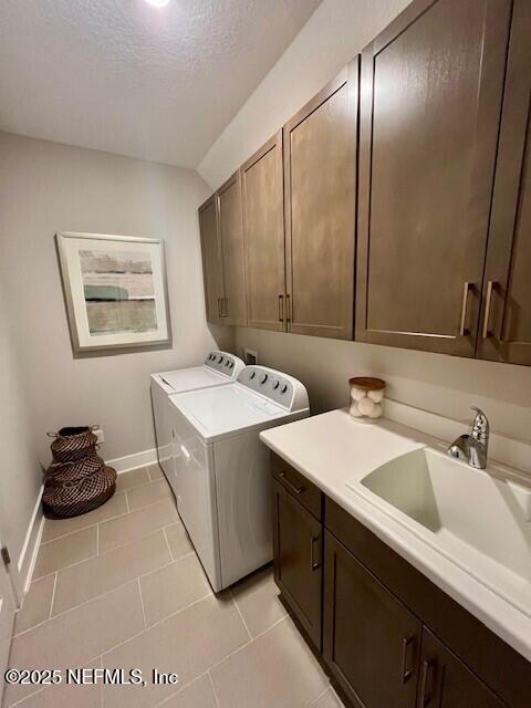 clothes washing area with independent washer and dryer, cabinets, sink, and light tile patterned floors